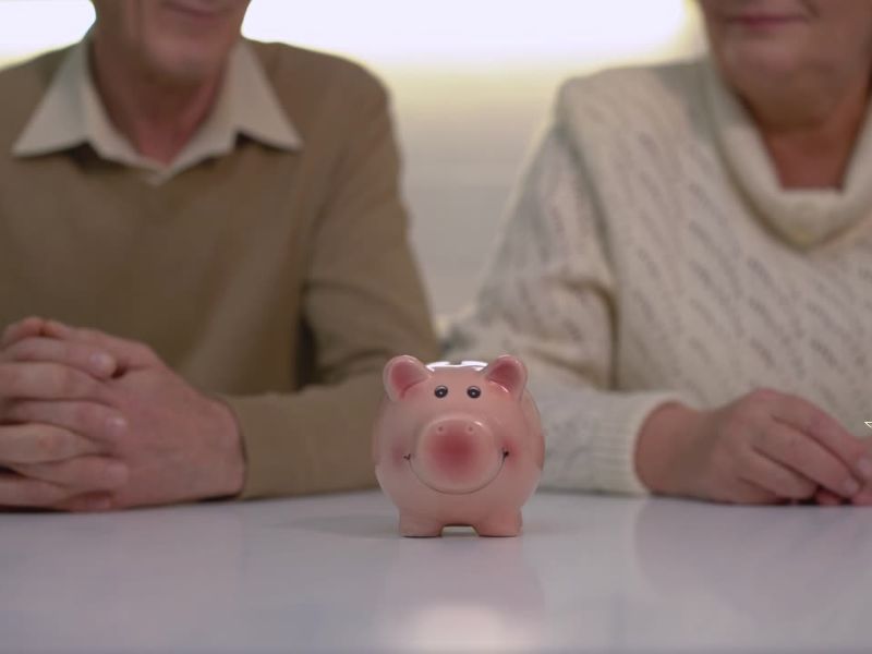 Dve osobe srednjih godina sede za stolom , na stolu kasica prasica roze boje