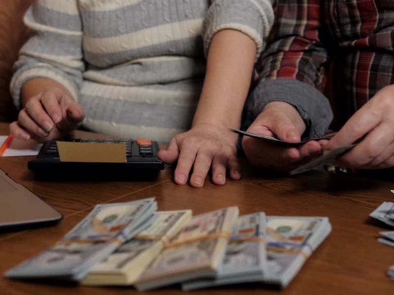 Dve osobe sede za stolom i računaju nešto, na stolu su kalkulatori i novac